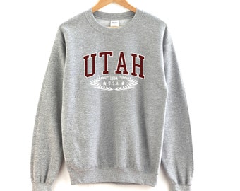 May include: Grey sweatshirt with a maroon "UTAH" graphic, white text "1994 U.S.A." and a laurel wreath.