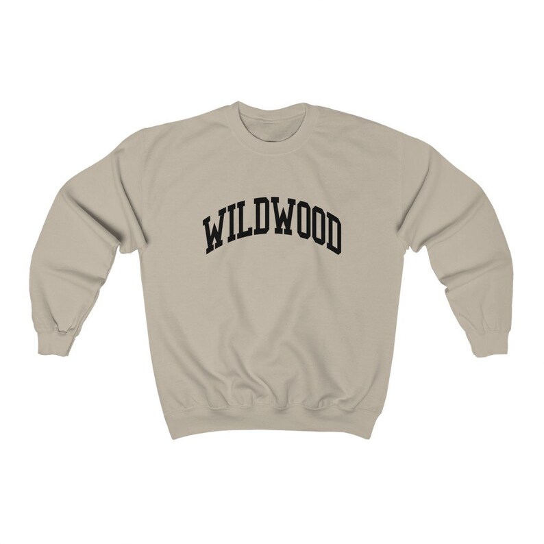 May include: A beige sweatshirt with the word "WILDWOOD" arched across the chest in bold, black letters. The sweatshirt has a crew neck and long sleeves, suitable for casual wear.