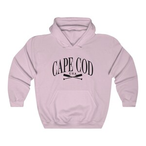 May include: A pink hooded sweatshirt with the text "CAPE COD USA" in black lettering and a pair of crossed oars underneath.