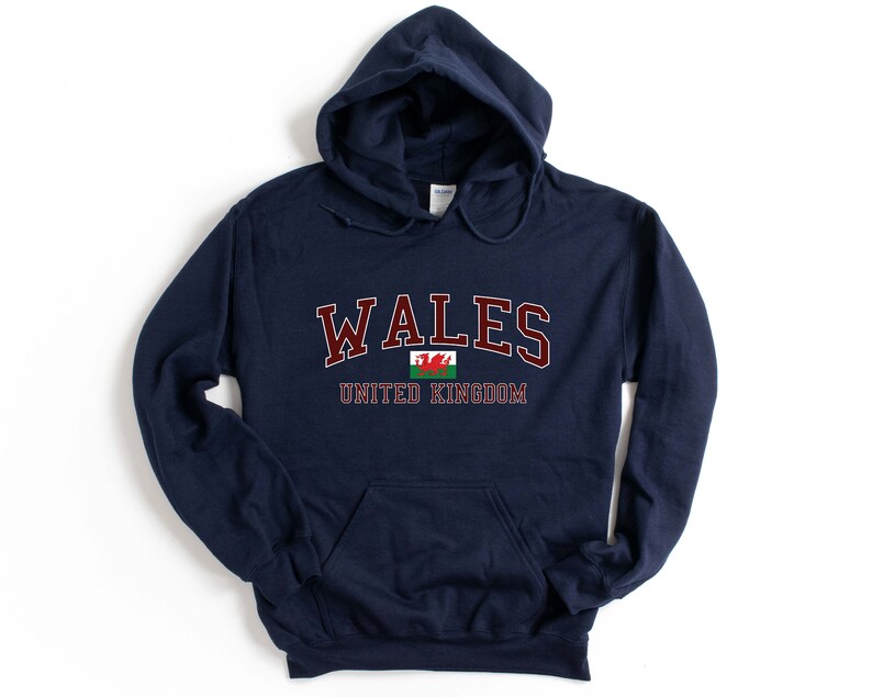 Puede incluir: Una sudadera con capucha azul marino con la palabra "WALES" en letras granate y la bandera galesa debajo. El texto "UNITED KINGDOM" est&aacute; impreso debajo de la bandera.
