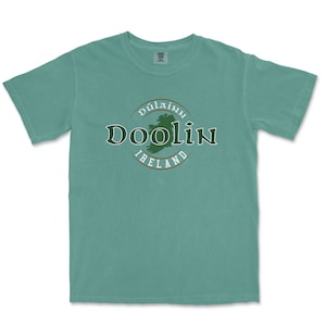 May include: A teal blue t-shirt with a green circle graphic featuring the text "Dúlainn Doolin Ireland" and a green outline of Ireland.
