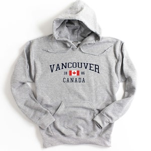 May include: A gray hooded sweatshirt with a navy blue print that says "Vancouver" with a Canadian flag and "18 86 CANADA" underneath.