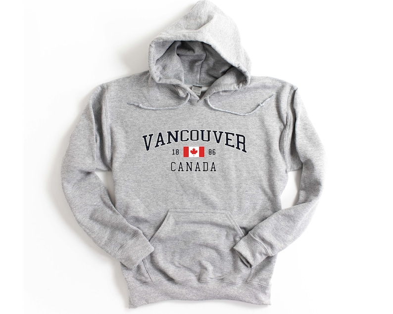 May include: A gray hooded sweatshirt with a navy blue print that says "Vancouver" with a Canadian flag and "18 86 CANADA" underneath.