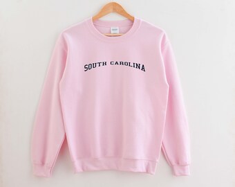 May include: A pink sweatshirt with the text "SOUTH CAROLINA" in navy blue lettering.