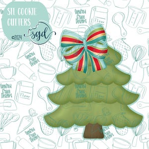 May include: A green Christmas tree cookie cutter with a red, white, and blue bow on top. The cutter is surrounded by a white background with a pattern of kitchen tools and the text "Sugared Grace Designs".