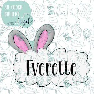 May include: A white cookie cutter with a bunny ear design and the name "Everette" in black text. The cookie cutter is on a white background with a pattern of blue kitchen tools.