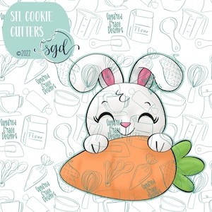 May include: A white bunny cookie cutter with pink inner ears and a smiling face, holding an orange carrot. The cutter has the text "STL Cookie Cutters" and "Sugared Grace Designs" on a white background with baking-themed illustrations.