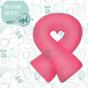 May include: Pink ribbon cookie cutter with a heart-shaped cutout in the center. The cutter is on a white background with a pattern of baking-themed illustrations in light blue.