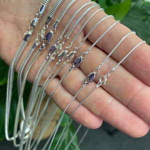 May include: A set of silver snake chains of varying lengths and widths. The chains are displayed on a hand, with the clasps visible.