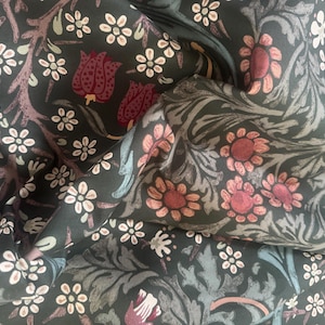 May include: A dark green fabric featuring a repeating pattern of stylized flowers and leaves in shades of muted pink, deep red, and light gray. The textile has a smooth texture with folds that create depth and shadows across the floral design.