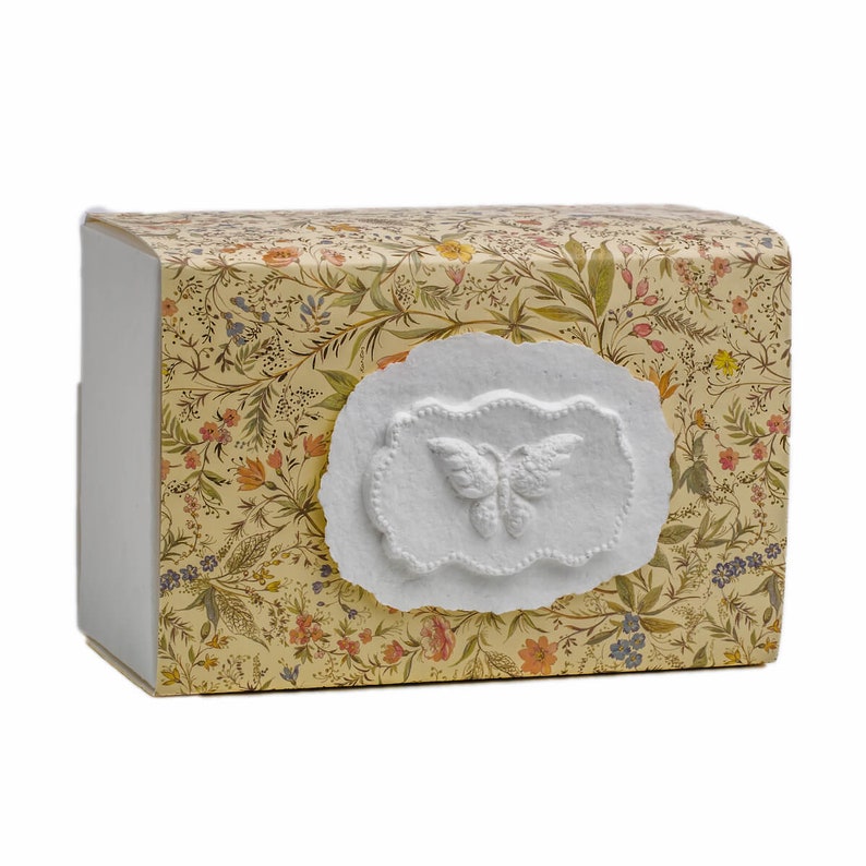 Op de afbeelding: Een kleine, rechthoekige doos met een bloemenpatroon en een wit reli&euml;f van een vlinder aan de voorkant.