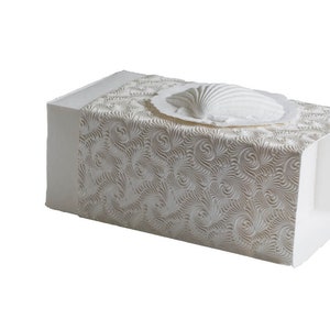K&ouml;nnte beinhalten: Wei&szlig;e, rechteckige Taschentuchbox mit strukturiertem, wirbelndem Muster. Obenauf befindet sich eine wei&szlig;e, muschelf&ouml;rmige Dekoration. Die Box hat ein sauberes, elegantes Design.