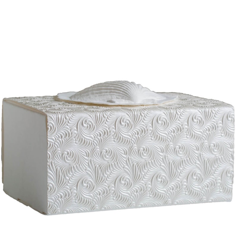 K&ouml;nnte beinhalten: Wei&szlig;e Taschentuchbox mit Muscheldesign. Die Box hat ein strukturiertes, wirbelndes Muster und eine rechteckige Form. Die Muschel ist ebenfalls wei&szlig; und verleiht dem Taschentuchhalter eine dekorative Note.