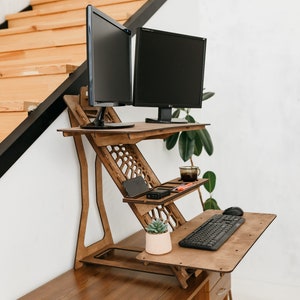 K&ouml;nnte beinhalten: Ein Stehpult aus Holz mit zwei schwarzen Computermonitoren, einer Tastatur, einer Maus, einer Topfpflanze und einer Tasse auf einem Regal. Der Schreibtisch ist in einem Heimb&uuml;ro eingerichtet.