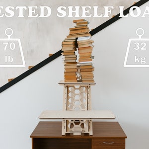 K&ouml;nnte beinhalten: Ein Stehpult aus Holz mit einem Wabenmuster und einem Regal. Das Regal ist mit einem Stapel B&uuml;cher gef&uuml;llt, und das Pult ist mit "TESTED SHELF LOAD" beschriftet und hat eine Gewichtsgrenze von 70 lb oder 32 kg.