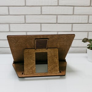 May include: A wooden laptop stand with a brown finish. The stand has a cutout for ventilation and a raised platform to elevate the laptop.