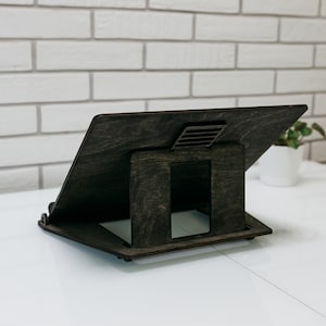 May include: A dark brown wooden laptop stand with a cutout for ventilation. The stand is angled to provide an ergonomic viewing position.