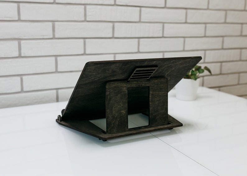 May include: A dark brown wooden laptop stand with a cutout for ventilation. The stand is angled to provide an ergonomic viewing position.