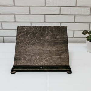 May include: A dark brown wooden stand with a black metal frame. The stand is designed to hold a book or tablet upright.