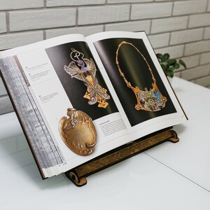 May include: An open book with a wooden stand, showcasing two pieces of jewelry. The jewelry is made of gold and features intricate designs with blue and green enamel. The book is titled "The Art Nouveau Jewelry of Ren&eacute; Lalique".
