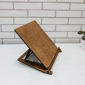 May include: A wooden book stand with a brown finish. The stand is angled to hold a book or tablet.