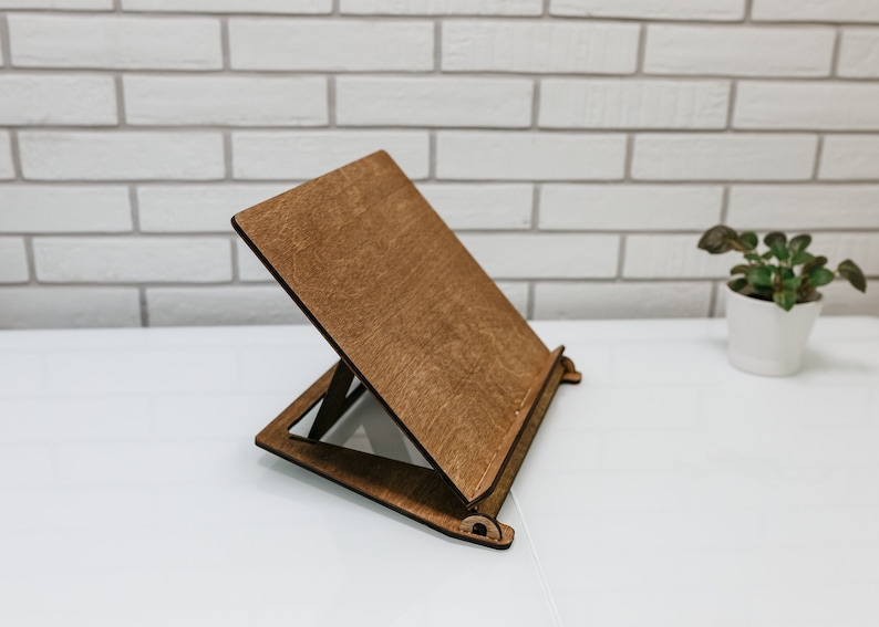 May include: A wooden book stand with a brown finish. The stand is angled to hold a book or tablet.