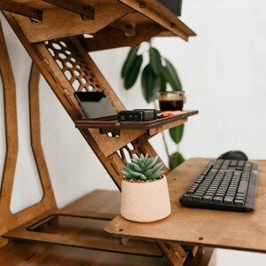K&ouml;nnte beinhalten: Ein Stehpult aus Holz mit einer Tastatur, einer Maus und einer kleinen Topfpflanze auf der Oberfl&auml;che. Der Schreibtisch hat ein Regal f&uuml;r ein Telefon oder Tablet und einen Becherhalter.