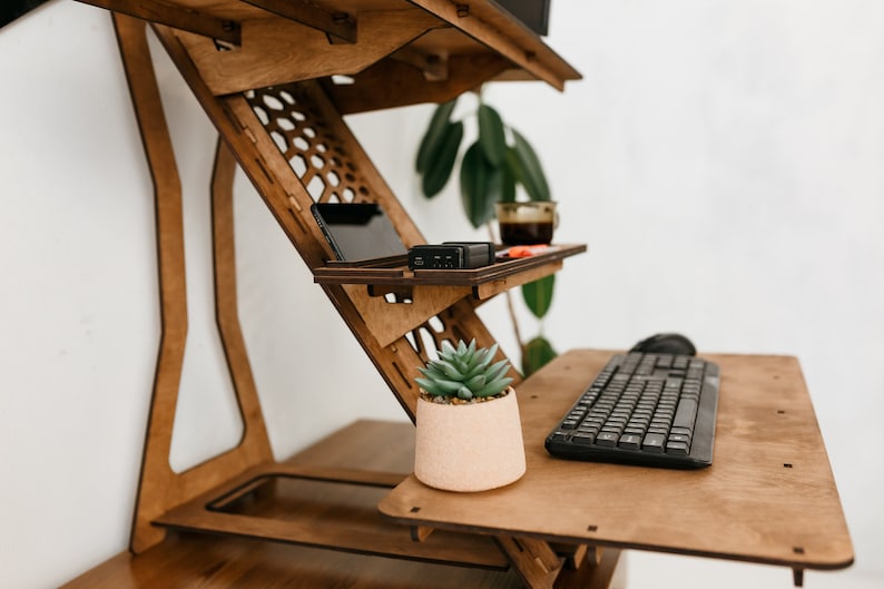 K&ouml;nnte beinhalten: Ein Stehpult aus Holz mit einer Tastatur, einer Maus und einer kleinen Topfpflanze auf der Oberfl&auml;che. Der Schreibtisch hat ein Regal f&uuml;r ein Telefon oder Tablet und einen Becherhalter.