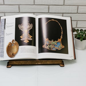 May include: A book stand with a book open to a page showing two pieces of jewelry. The jewelry is made of gold and has a detailed design. The book stand is made of wood and has a dark brown finish.