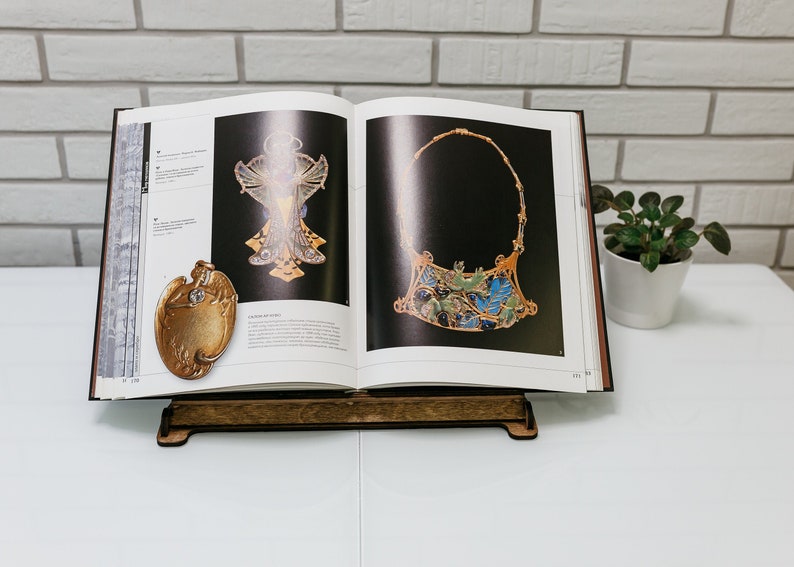 May include: A book stand with a book open to a page showing two pieces of jewelry. The jewelry is made of gold and has a detailed design. The book stand is made of wood and has a dark brown finish.