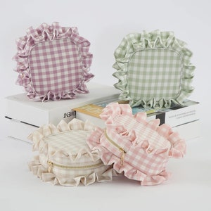 May include: Three gingham-patterned bags in pink, green, and cream with ruffled edges. Two are square, and one is round with a gold zipper. The bags are arranged on a white surface.