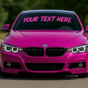 May include: A vibrant magenta car with the text "YOUR TEXT HERE" across the windshield. The car has a black grille, headlights with white accents, and the BMW logo on the hood. The car is parked on a paved surface.