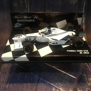 May include: A 1/18 scale diecast model car of the Tyrrell Ford 025 driven by Mika Salo in the 1998 Formula One season. The car is white and black and is displayed on a black and white chequered base with the words "Paul's Model Art" and "Minichamps" on the box.