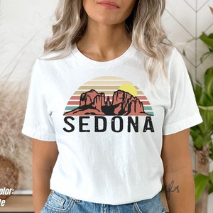 May include: White t-shirt with a retro sunset graphic featuring red rock formations and the word "SEDONA" in black text.