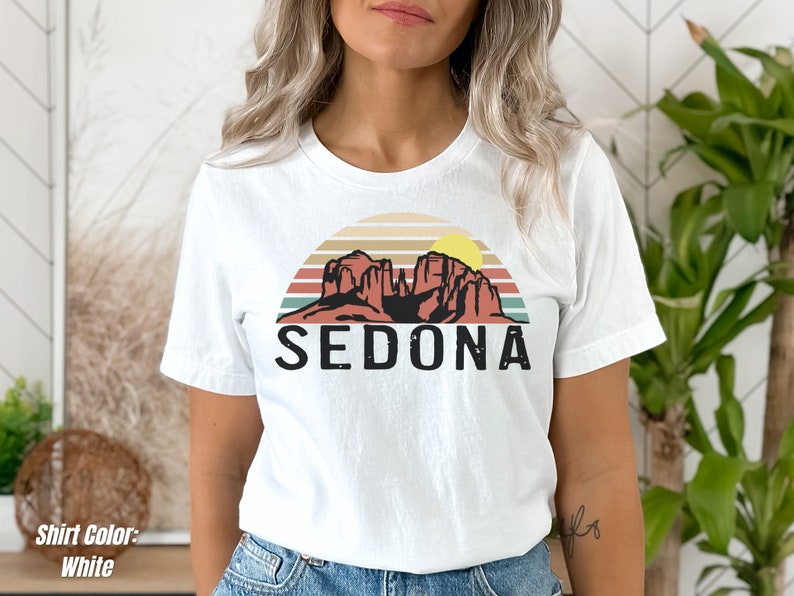 May include: White t-shirt with a retro sunset graphic featuring red rock formations and the word "SEDONA" in black text.