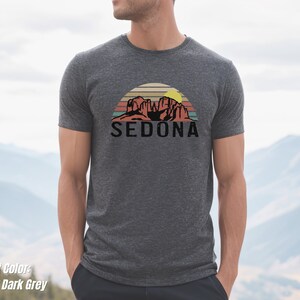 May include: Heather dark grey t-shirt with a vintage-style graphic of red rock formations and a sunset with the word "SEDONA" in black text.