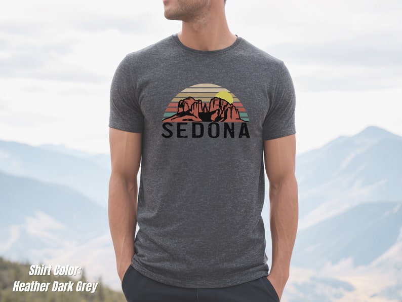 May include: Heather dark grey t-shirt with a vintage-style graphic of red rock formations and a sunset with the word "SEDONA" in black text.