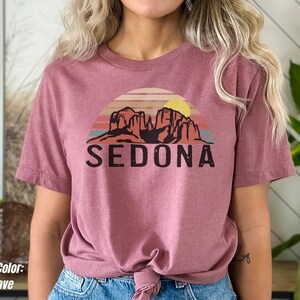 May include: A mauve t-shirt with a graphic of a sunset over red rock formations and the word "SEDONA" printed in black.