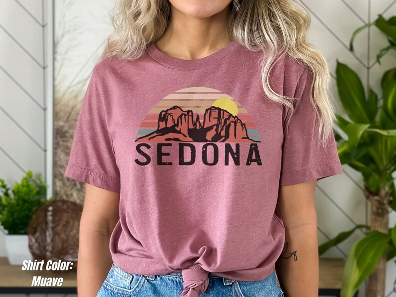 May include: A mauve t-shirt with a graphic of a sunset over red rock formations and the word "SEDONA" printed in black.