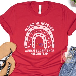 Puede incluir: Camiseta roja con un diseño de arcoíris blanco y el texto "In April we wear red Autism Acceptance #RedInstead".