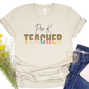 Puede incluir: Una camiseta beige con el texto "Pre K Teacher" en letra negra. La palabra "Teacher" est&aacute; en estampado de leopardo con rayas de colores detr&aacute;s.