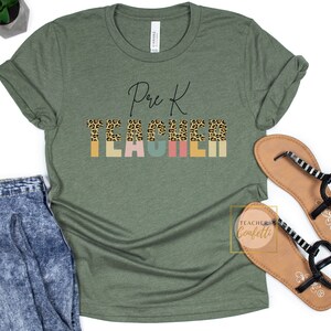 Puede incluir: Camiseta verde con el texto "Pre K Teacher" en letras negras. La palabra "Teacher" est&aacute; formada por letras de estampado de leopardo con fondos coloridos.