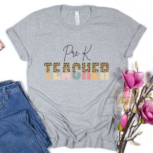 Puede incluir: Una camiseta gris con el texto "Pre K Teacher" en letra negra. La palabra "Teacher" est&aacute; formada por letras de estampado de leopardo con un fondo colorido.