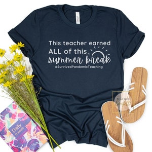 May include: A dark blue t-shirt with the text "This teacher earned ALL of this summer break #SurvivedPandemicTeaching" in white. The shirt features a white sun graphic.