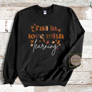 May include: Black sweatshirt with the text "fall in love with learning" in white and brown lettering. The text is surrounded by small brown, orange, and red leaf illustrations.