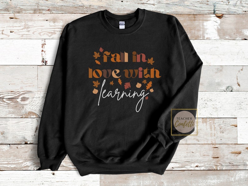 May include: Black sweatshirt with the text "fall in love with learning" in white and brown lettering. The text is surrounded by small brown, orange, and red leaf illustrations.