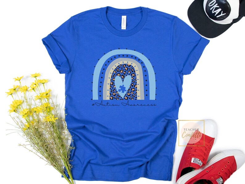 May include: A royal blue t-shirt with a rainbow design featuring a heart with a puzzle piece inside. The text "#Autism Awareness" is printed below the rainbow.
