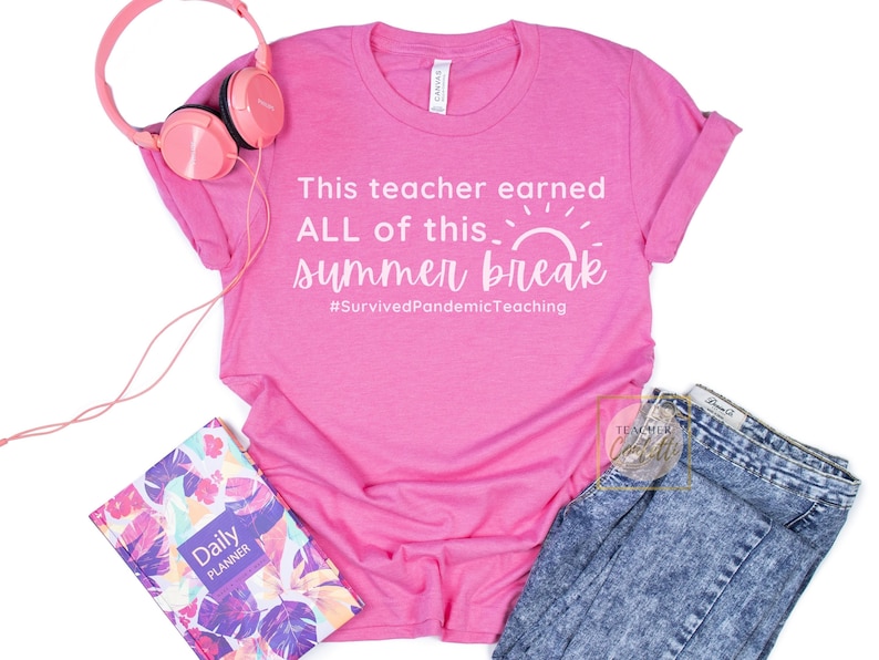 May include: Pink t-shirt with white text that reads "This teacher earned ALL of this... summer break #SurvivedPandemicTeaching". The shirt is laying on a white surface with a pink headband, a planner, and a pair of blue jeans.