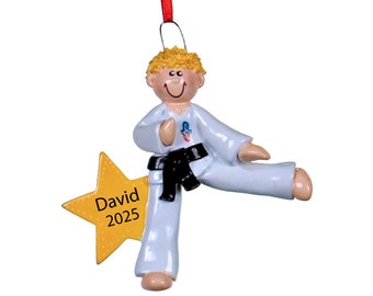May include: A personalized Christmas ornament featuring a cartoon boy in a white karate uniform with a black belt, kicking with his right leg. He is smiling and has blonde hair. A yellow star with the text "David 2025" is behind him.
