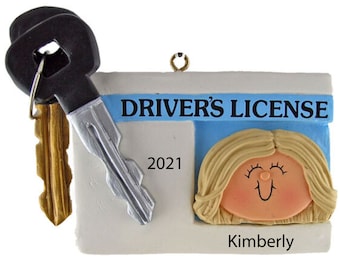 May include: A white and blue driver's license ornament with a cartoon woman's face and the text "DRIVER'S LICENSE" and "Kimberly". The ornament also includes two keys, one black and one gold.